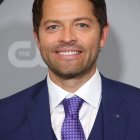 Smiling man in navy blue suit with stubble on grey backdrop