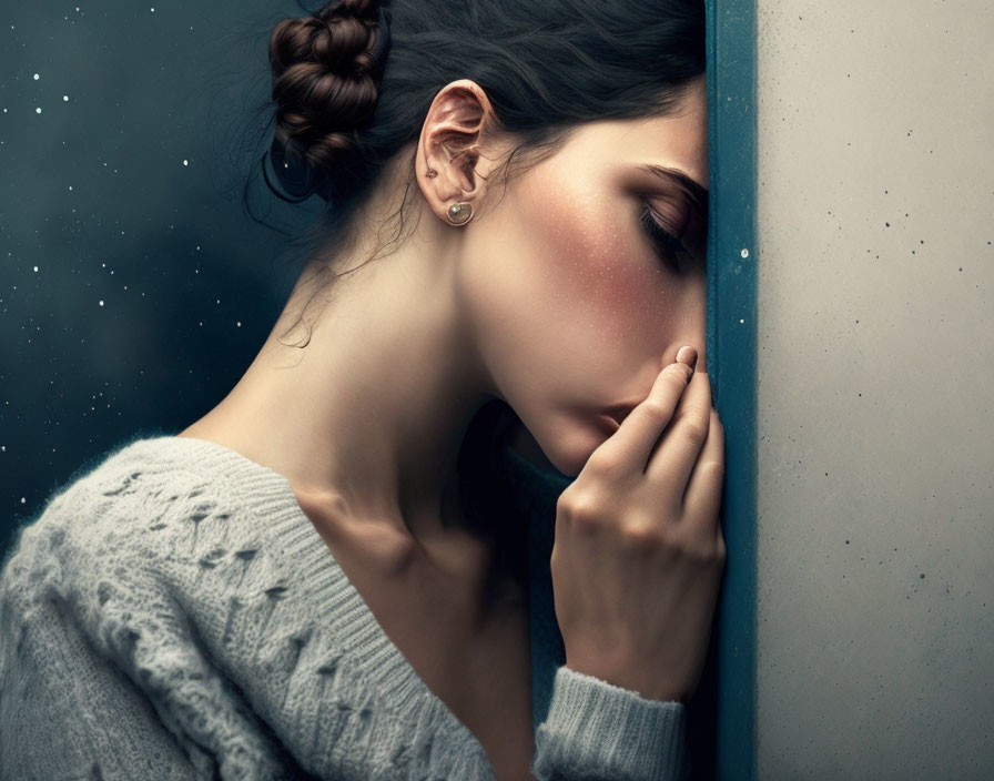 Woman in gray sweater with bun hairstyle gazes out misted window