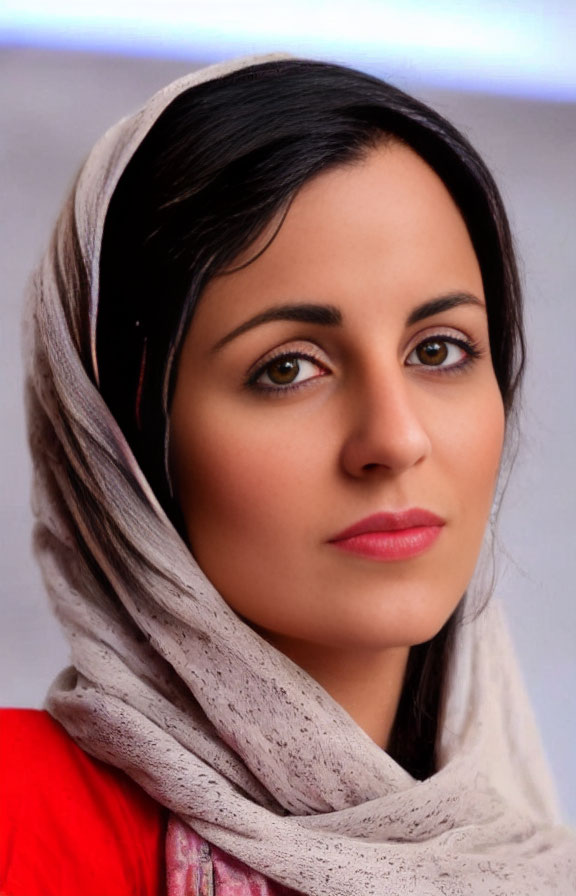 Dark-haired woman in red top and head scarf gazes calmly forward.