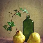 Creamy white flowers and yellow quinces in green vase on warm-toned backdrop