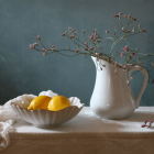 White porcelain pitcher with golden handle and pink flowers next to oranges on embroidered cloth