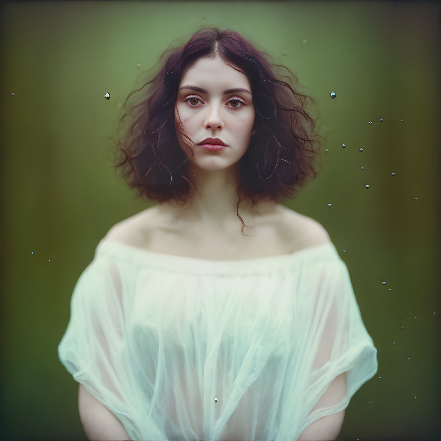 Dark-haired woman in sheer white top against green background