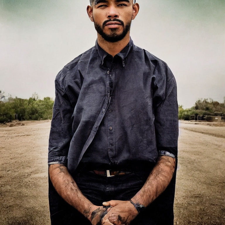 Bearded man with tattoos in dark shirt under overcast sky