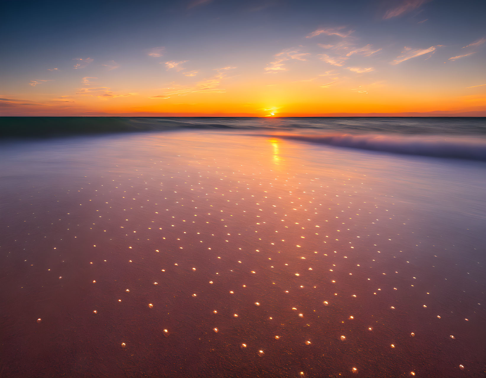 Vibrant sunset beach scene with orange and blue skies, waves, and glistening sand.