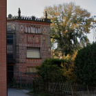 Old house with ornate balconies, tree, brick wall, greenery, metal fence