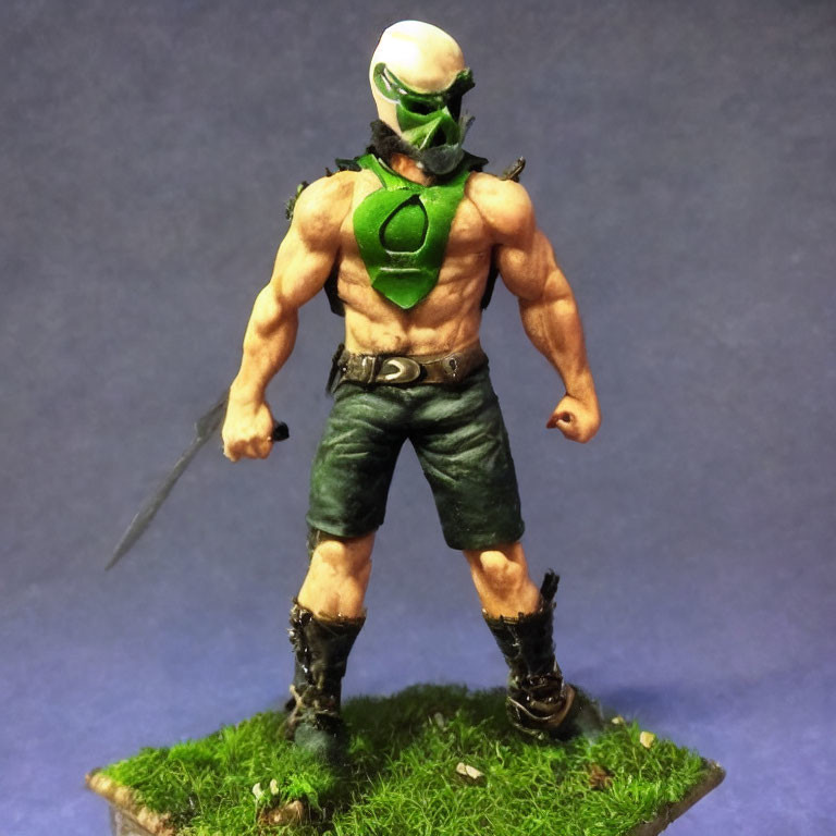 Muscular figurine with green mask and knife on grassy base