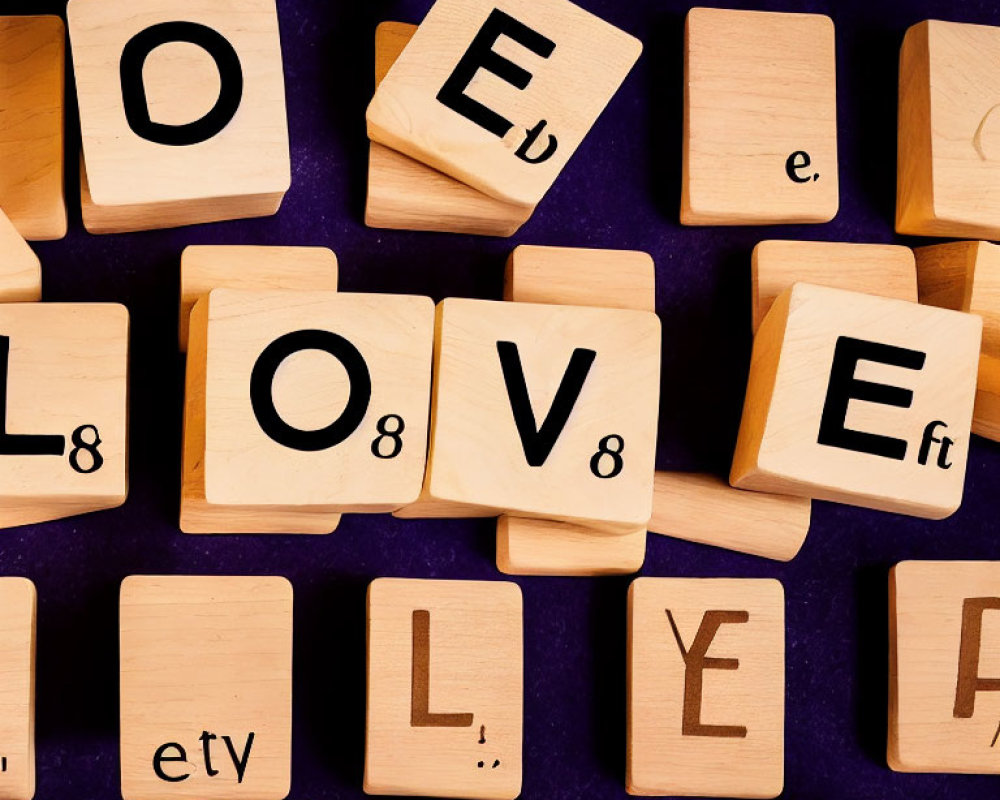 Wooden blocks spell "LOVE" on purple surface with scattered letter and number tiles