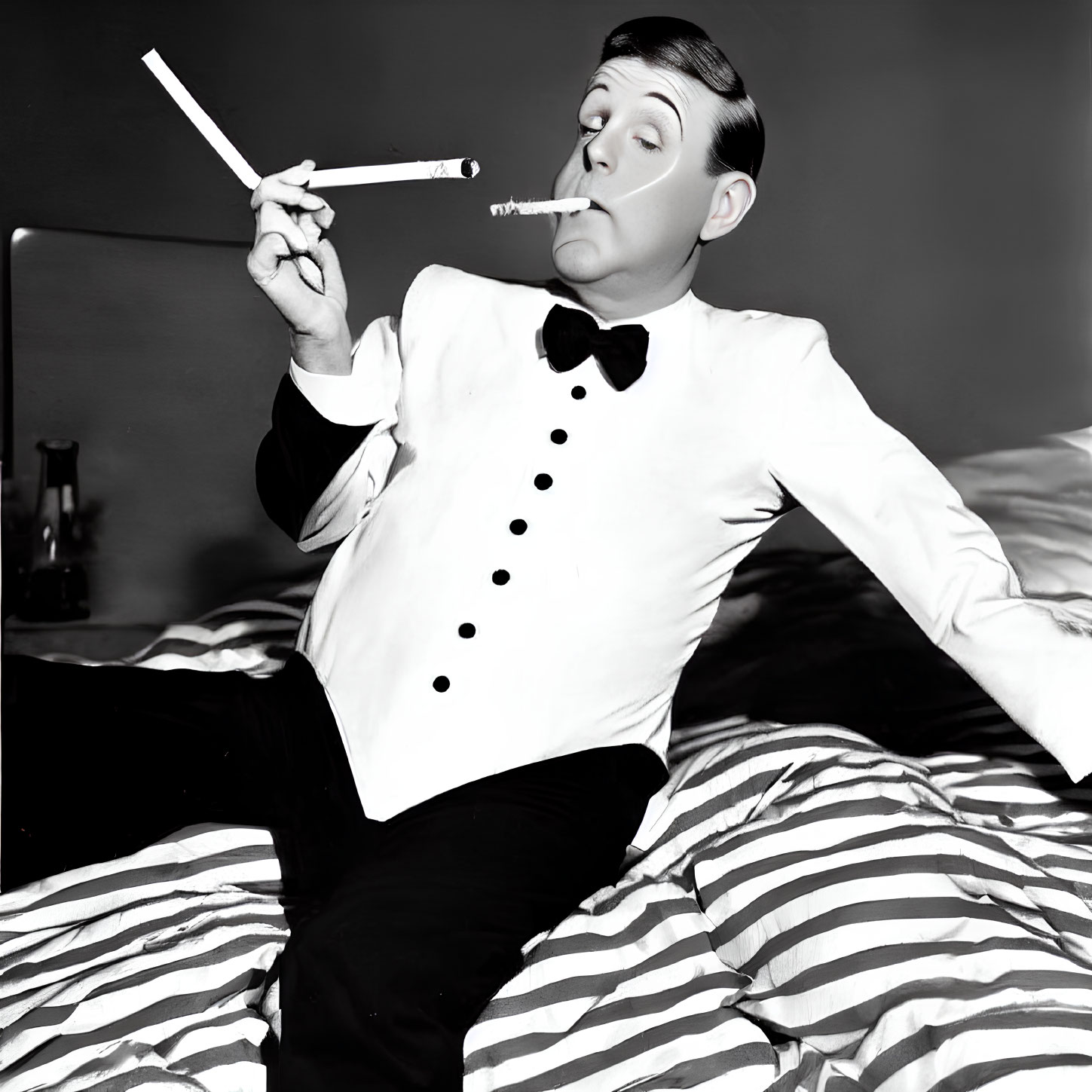 Monochrome image: man in tuxedo with long cigarette holder on striped bed