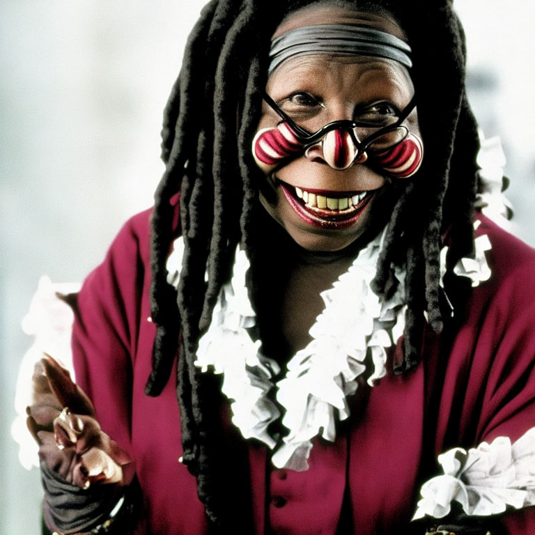 Clown-like person with face paint, glasses, dreadlocks, and ruffled collar gesturing.