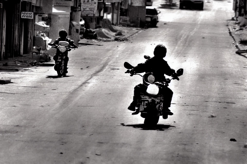 Children riding motorbikes on deserted street with buildings and debris in black and white.