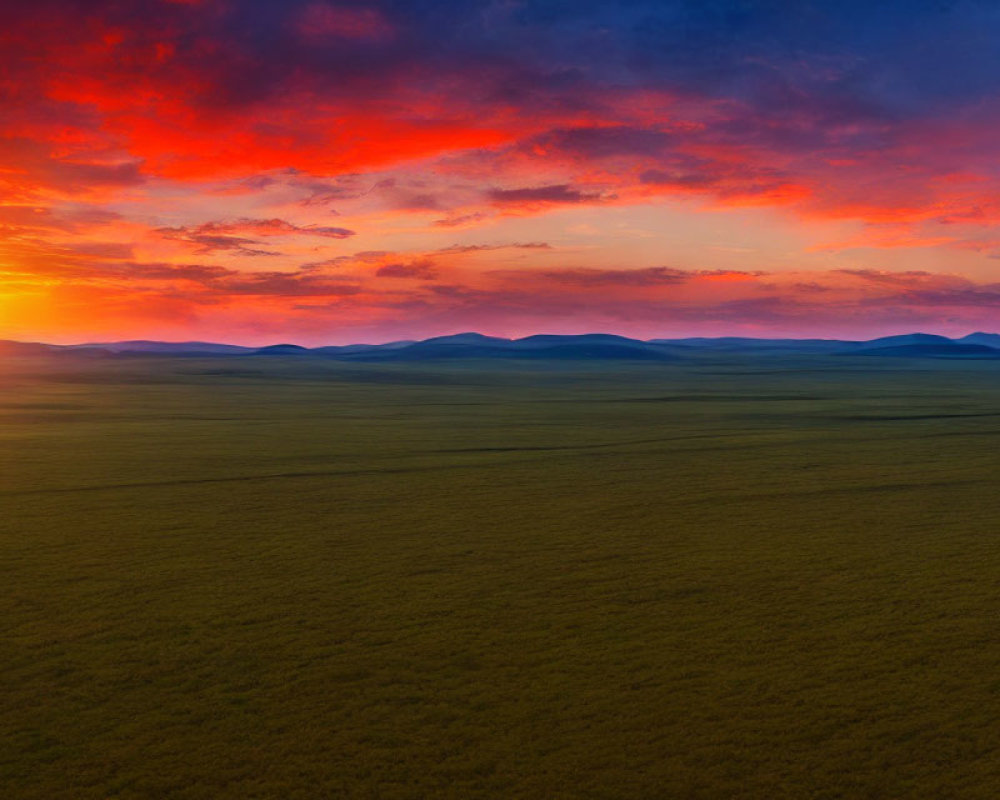 Colorful sunrise over green plain with distant hills