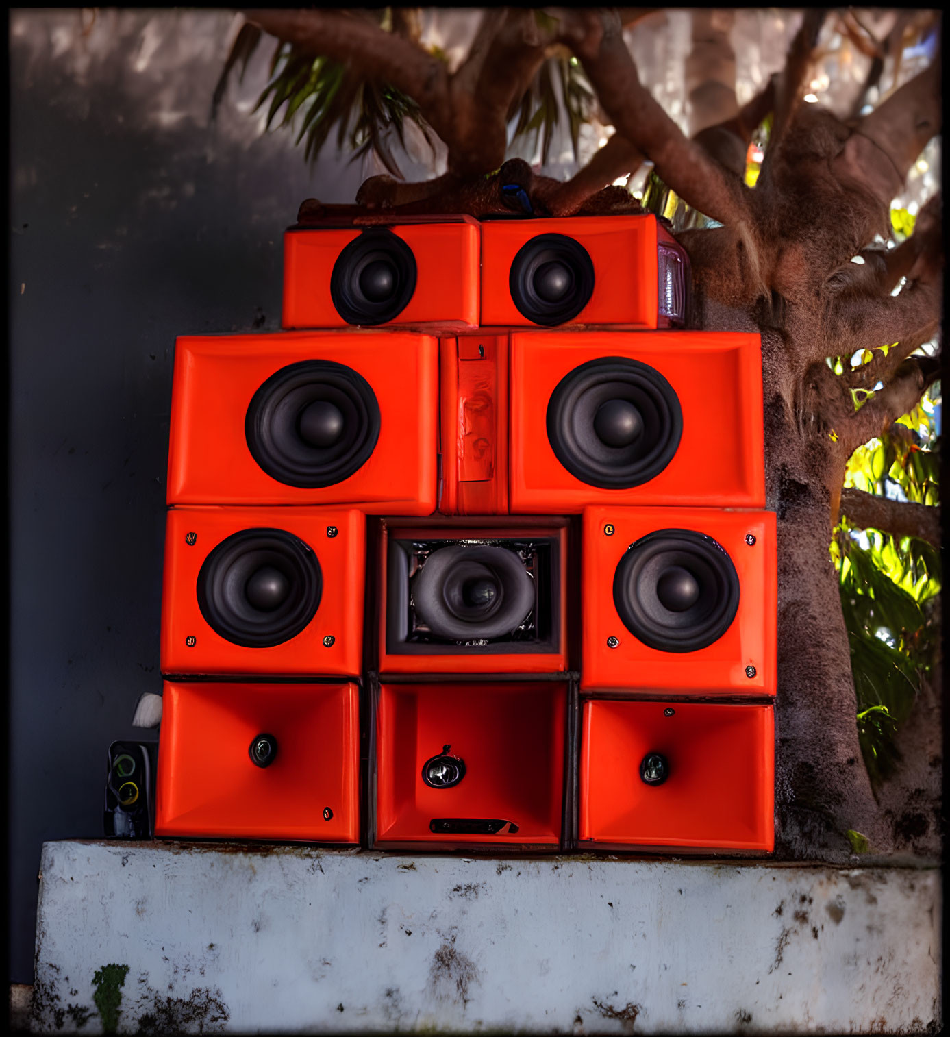 Vibrant orange speakers under shady tree create outdoor musical vibe