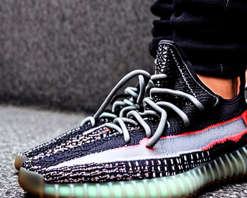 Person's Feet in Stylish Black and Multicolored Knit Sneakers on Gray Pavement