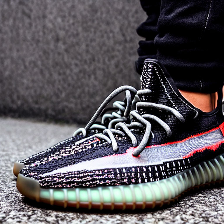 Person's Feet in Stylish Black and Multicolored Knit Sneakers on Gray Pavement