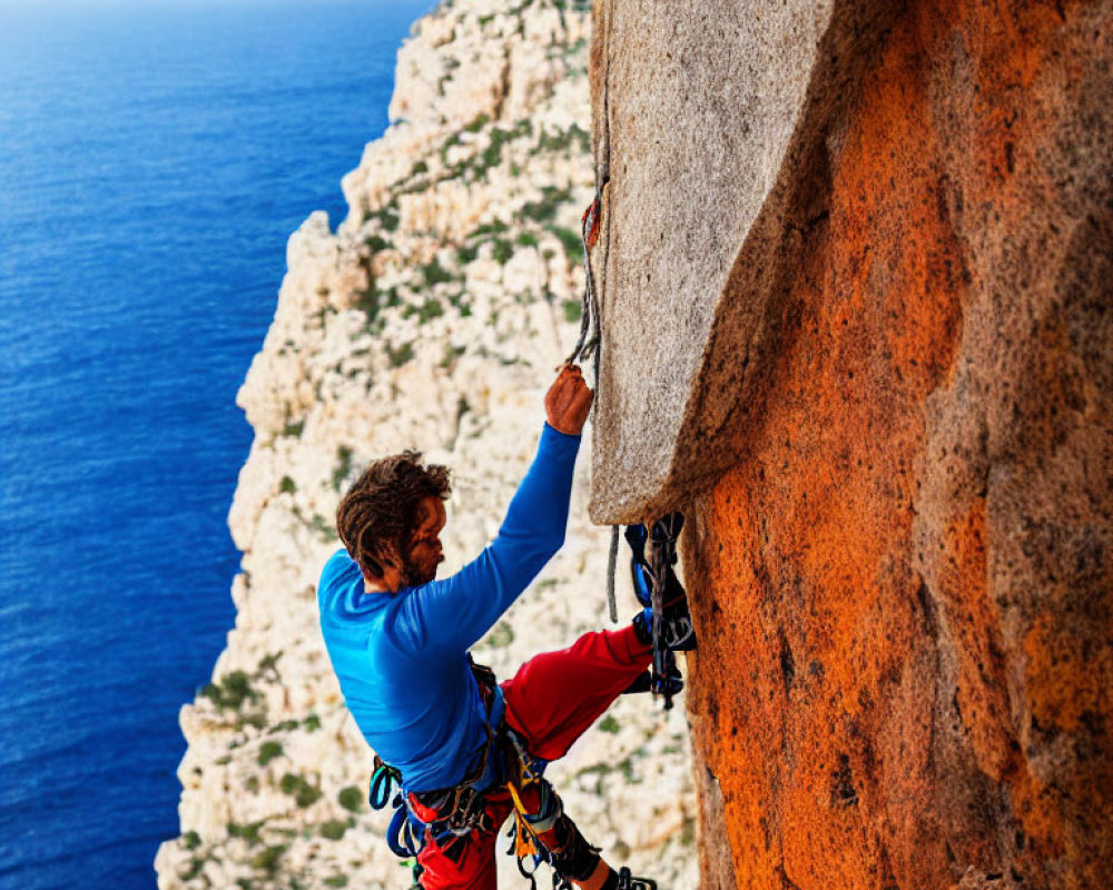 Blue climber scaling steep orange rock near vast sea with secure gear.