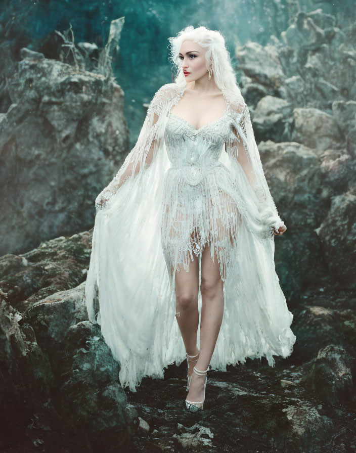 Woman in intricate white lace gown standing on mossy rocks in misty surroundings