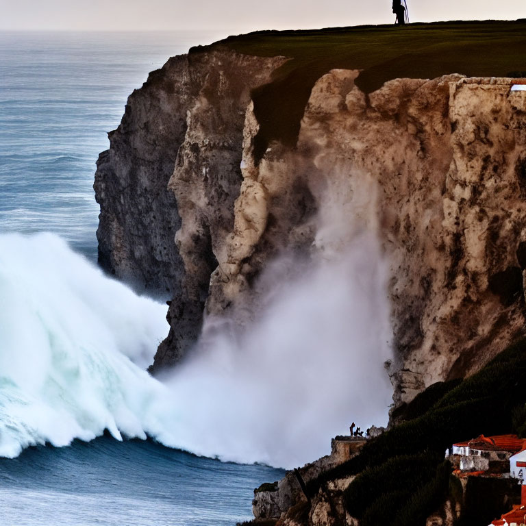 Person standing on towering cliff overlooking crashing waves and coastal buildings