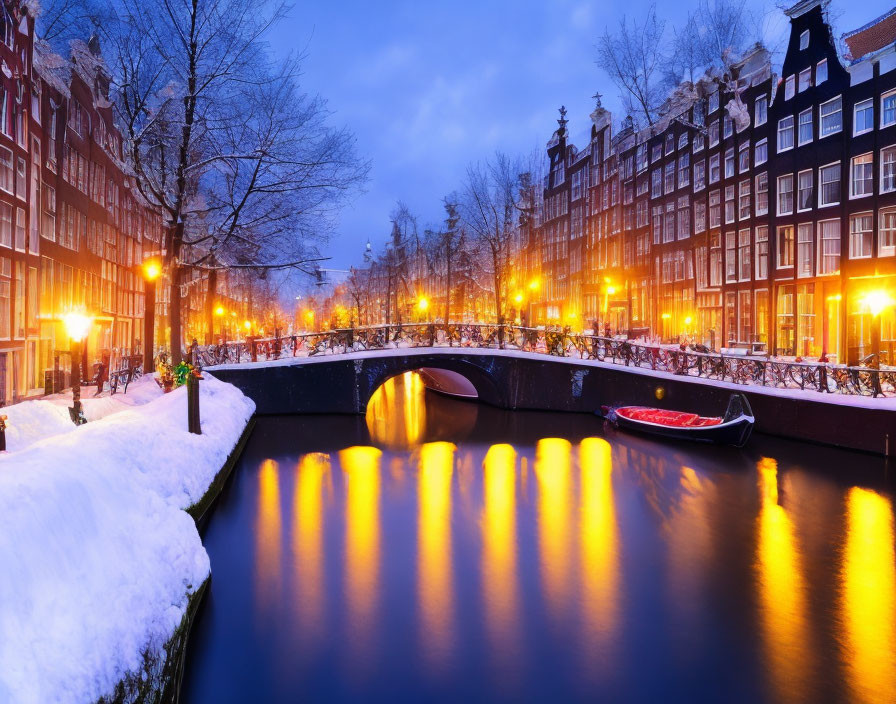 Snow-lined canal in Amsterdam with illuminated townhouses and bridge at winter dusk