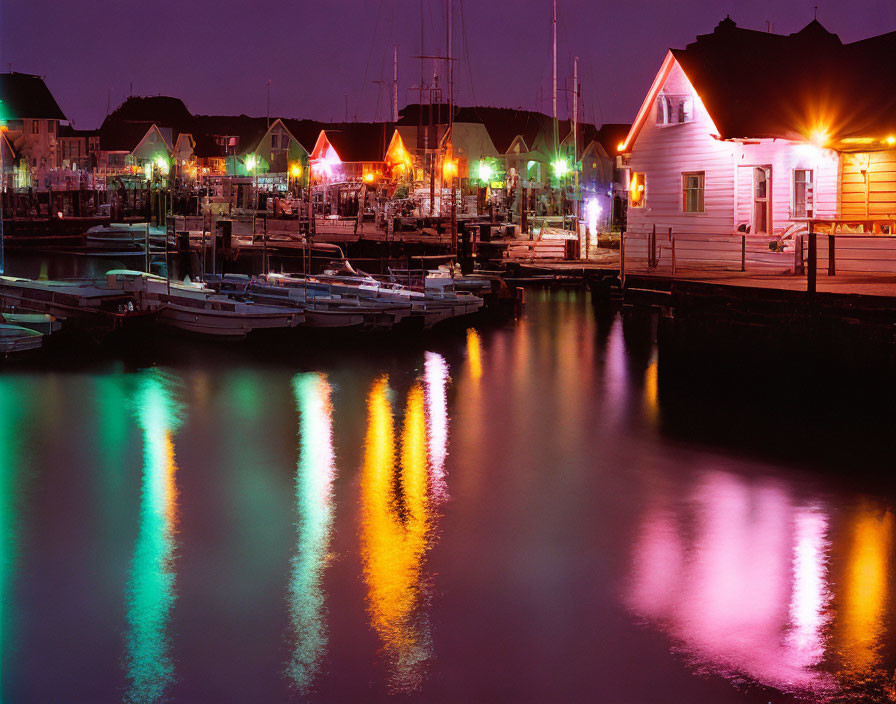 Night scene: tranquil marina with docked boats, colorful lights, and quaint houses