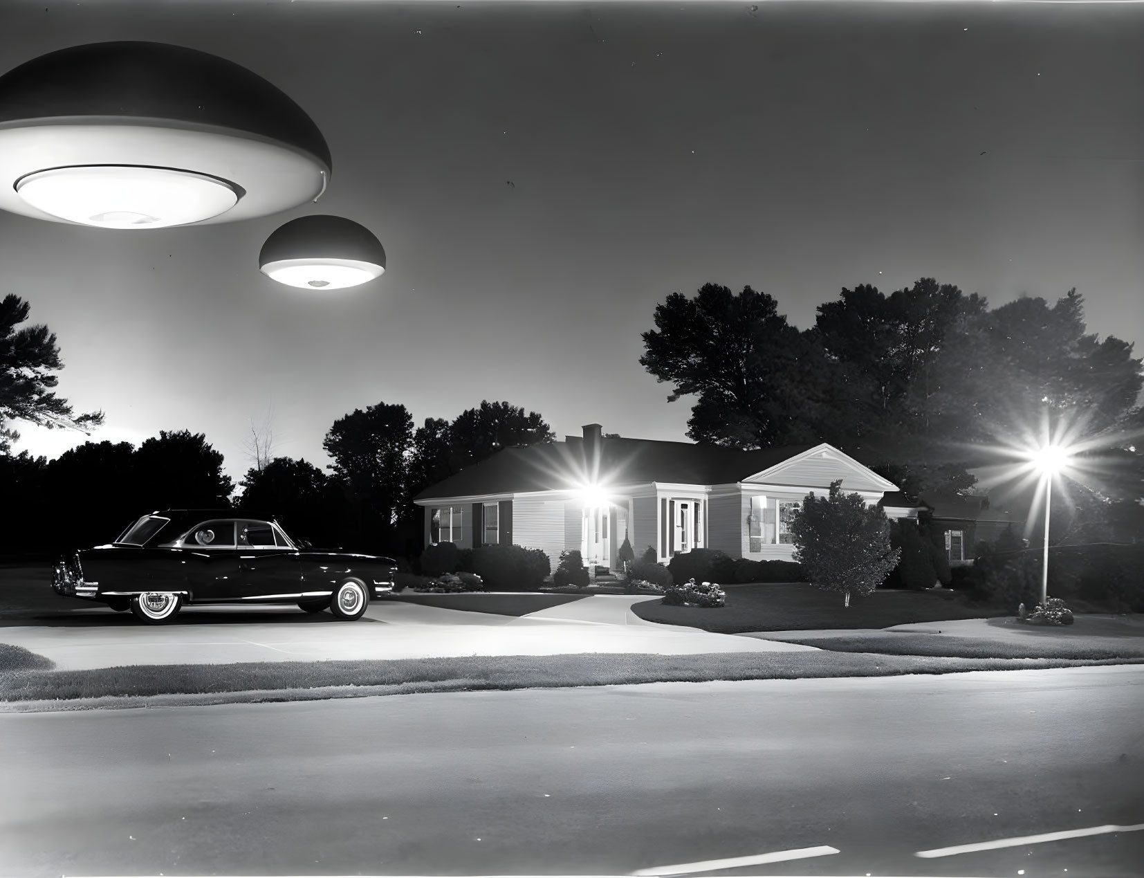 Vintage black and white photo of classic car, house, lights, and UFOs at night