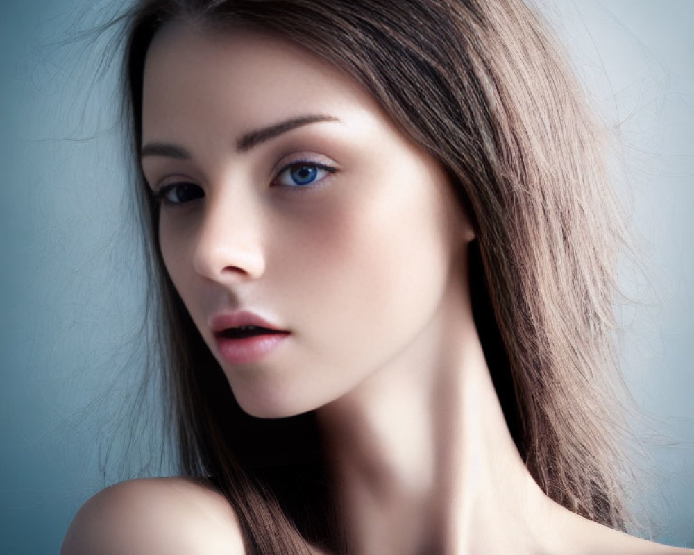 Young woman with blue eyes, smooth skin, and brown hair against blurred blue background