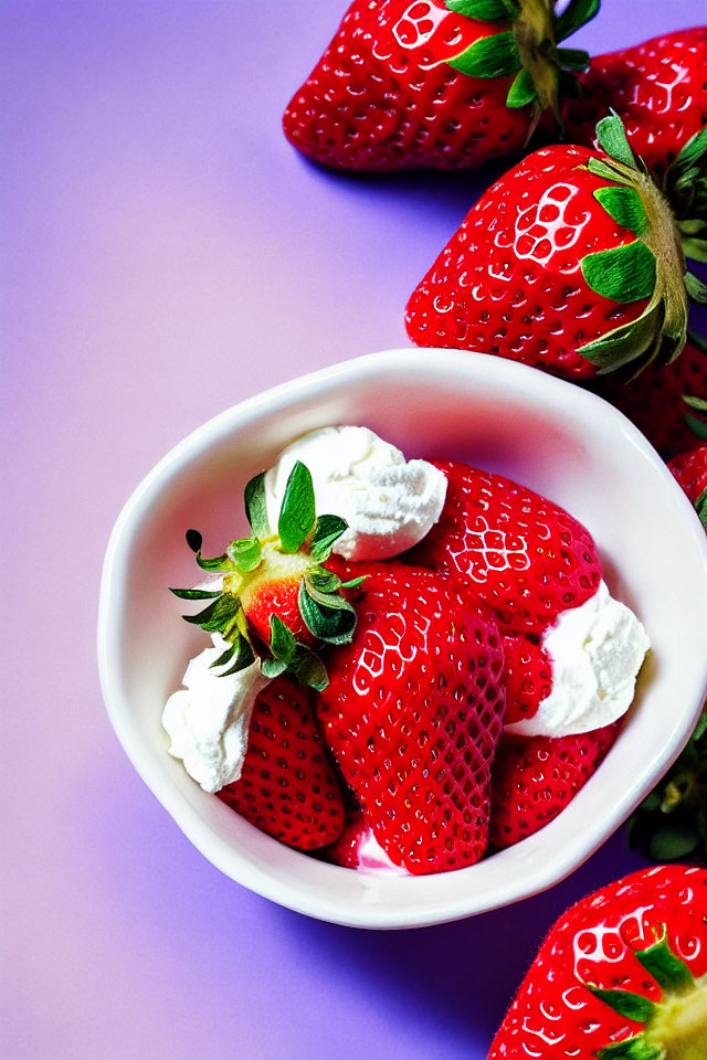 Ripe strawberries and whipped cream in white bowl on purple backdrop