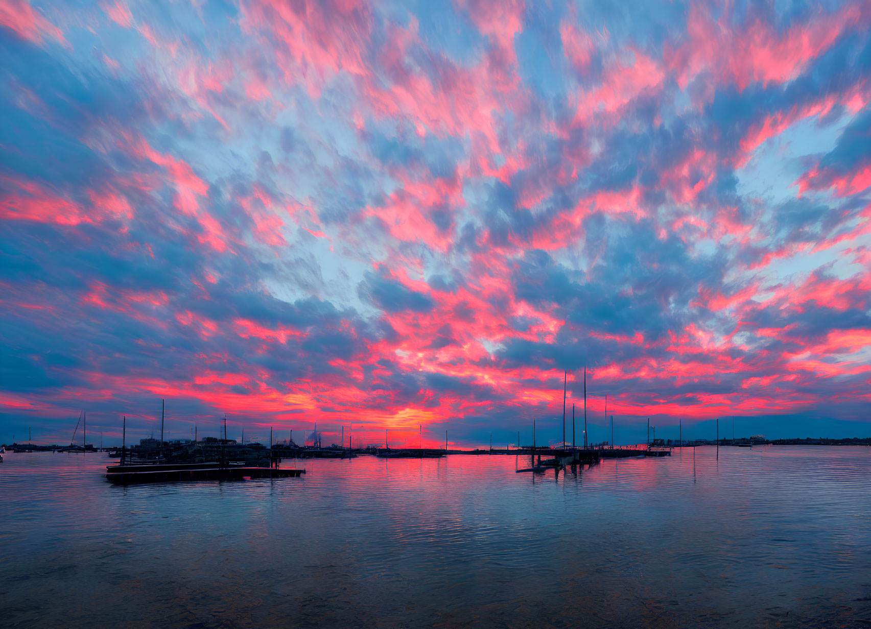 Fiery red and blue sunset over calm bay with sailboats and jetty