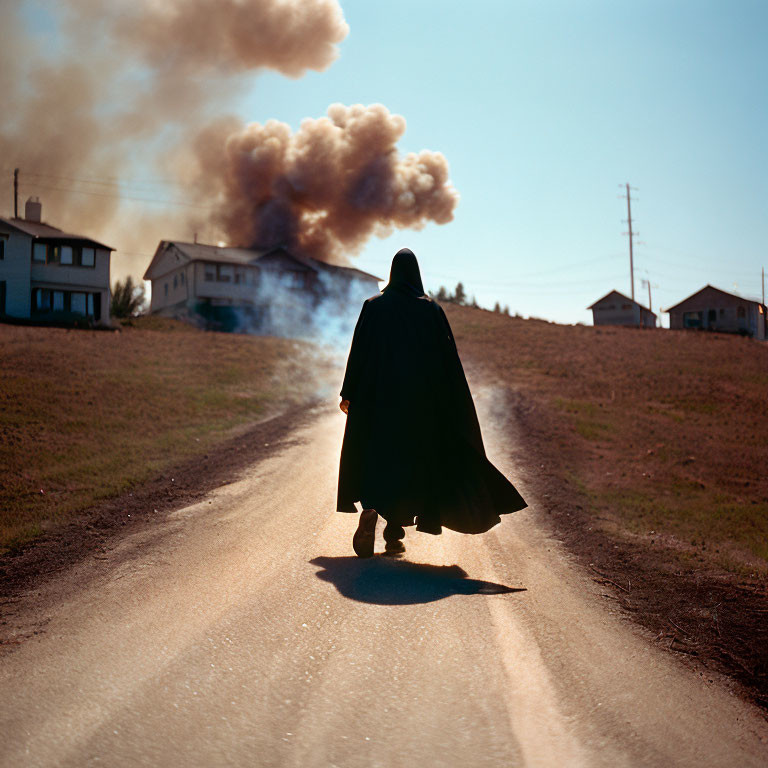 Person in Cape Walks Toward Smoke on Rural Road