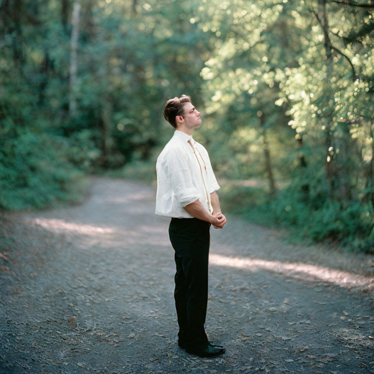 Man in white shirt and dark pants at forest path fork, looking upwards.