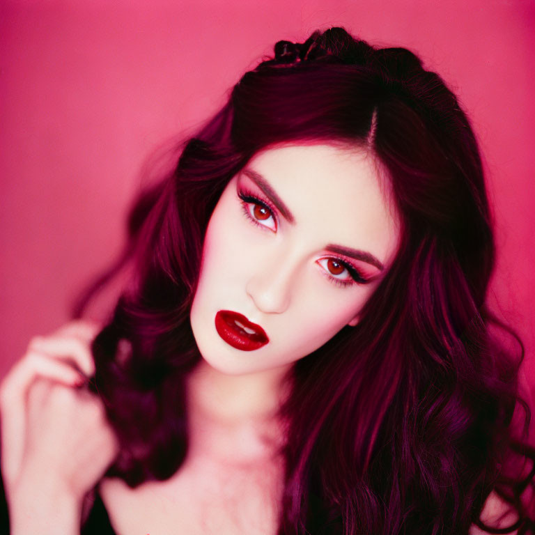 Dark-haired woman with red lipstick and eyeshadow on pink background.