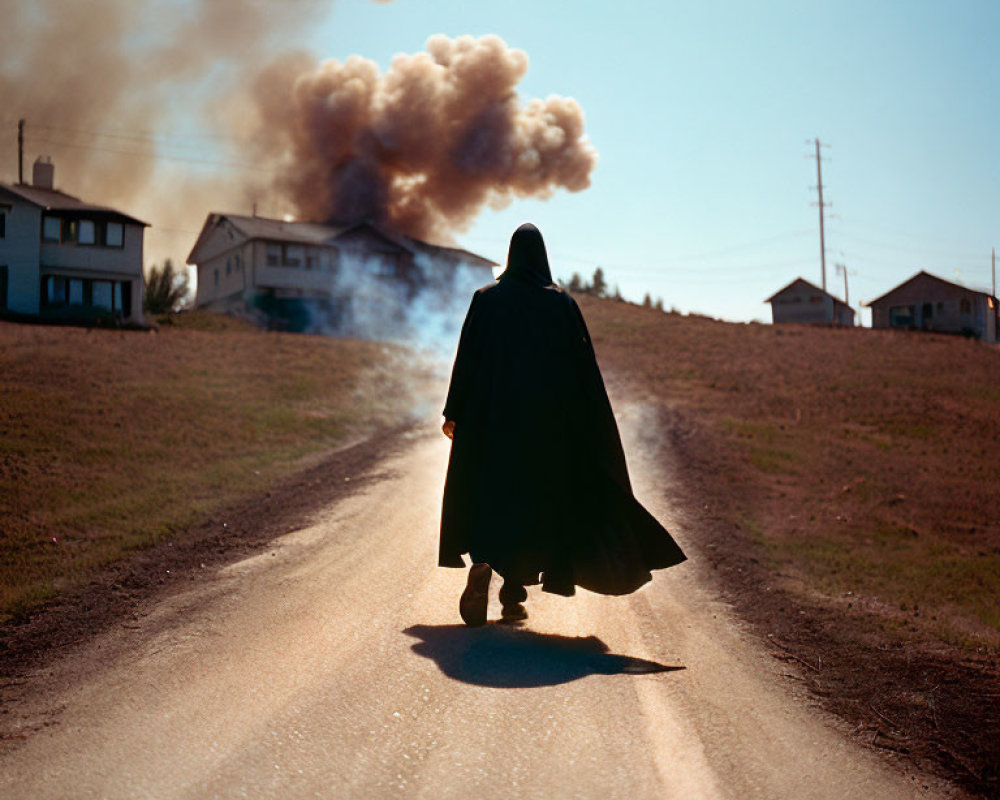 Person in Cape Walks Toward Smoke on Rural Road