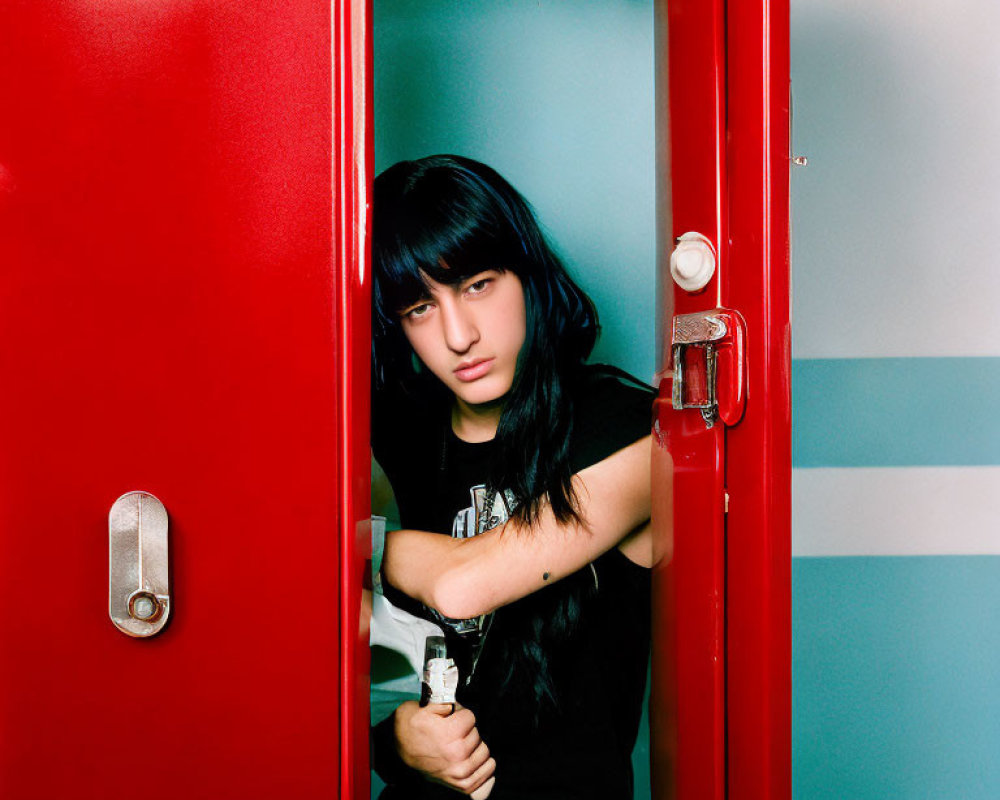 Serious person with black hair and fringe behind vibrant red door