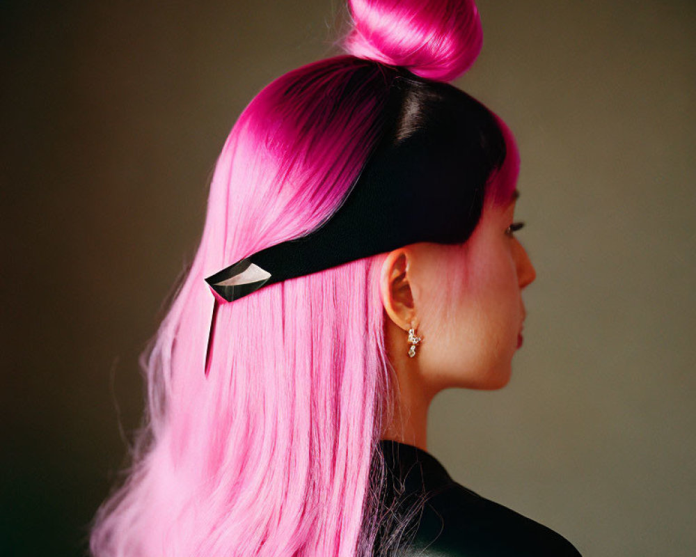 Profile of person with vibrant pink hair in top bun, black headband & clip