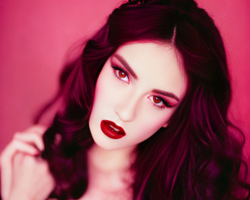 Dark-haired woman with red lipstick and eyeshadow on pink background.