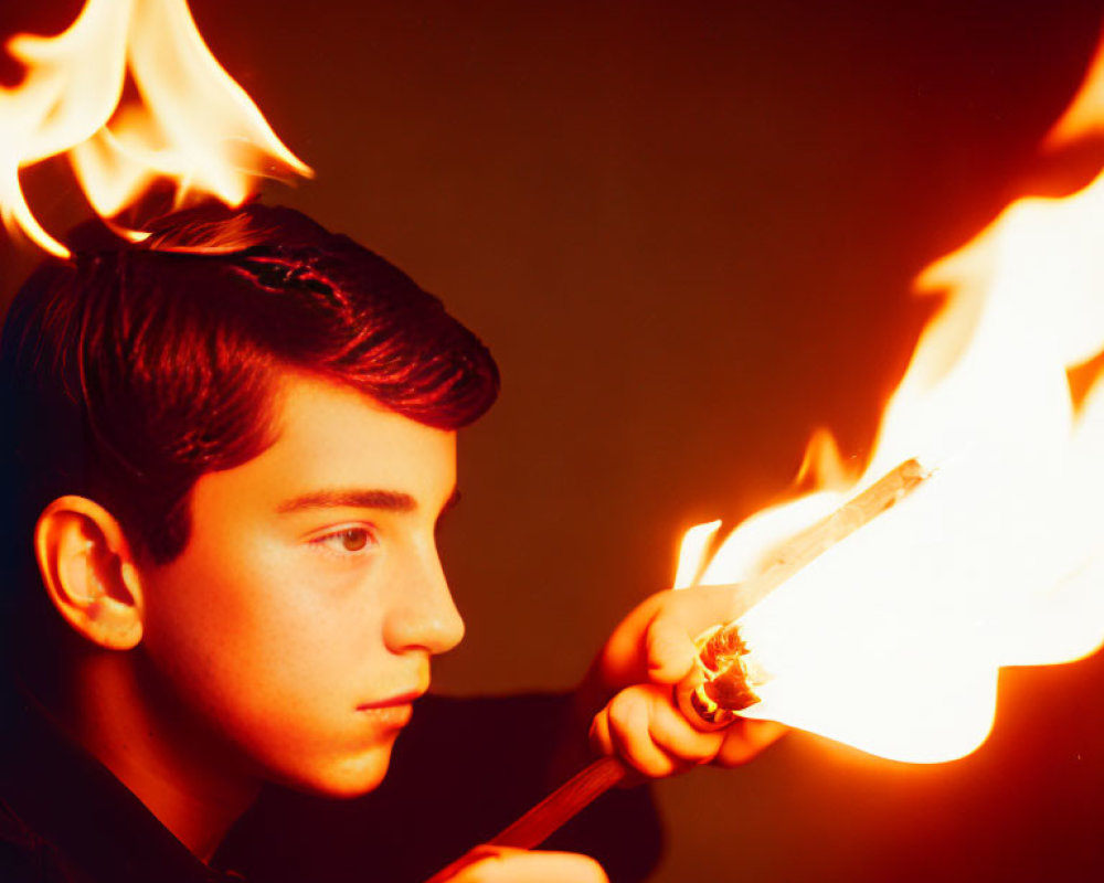 Person holding flaming stick against dark background.