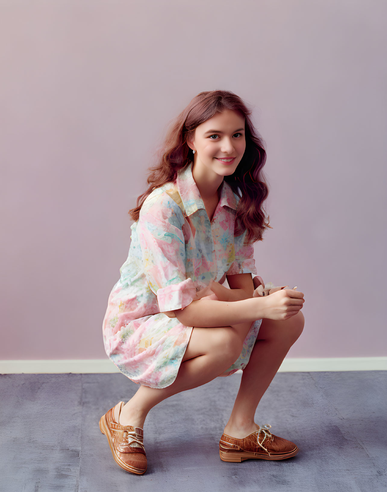 Smiling young woman in pastel tie-dye shirt dress and brown loafers on purple backdrop