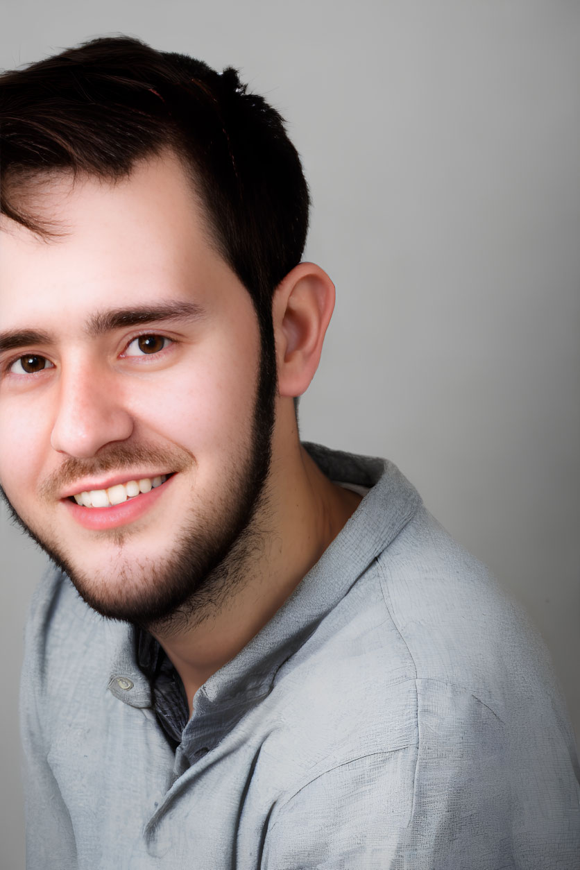 Smiling young man with stubble in light grey shirt on grey background