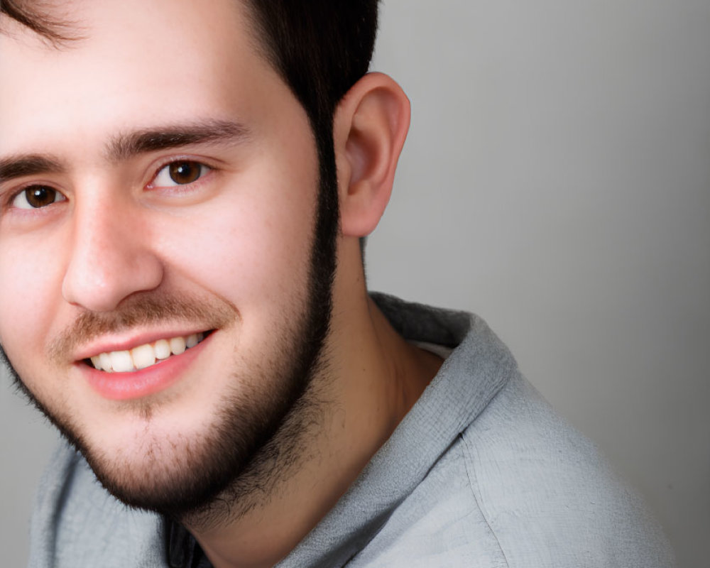 Smiling young man with stubble in light grey shirt on grey background