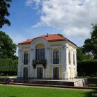 Fairytale-like building with golden spire in lush park with pine trees