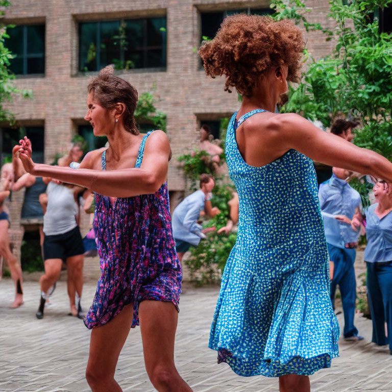 Women in summer dresses dancing outdoors with background figures.