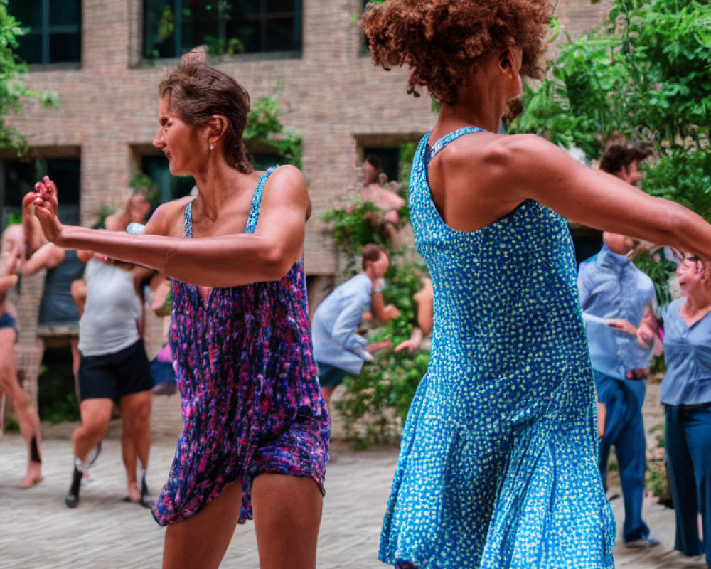 Women in summer dresses dancing outdoors with background figures.