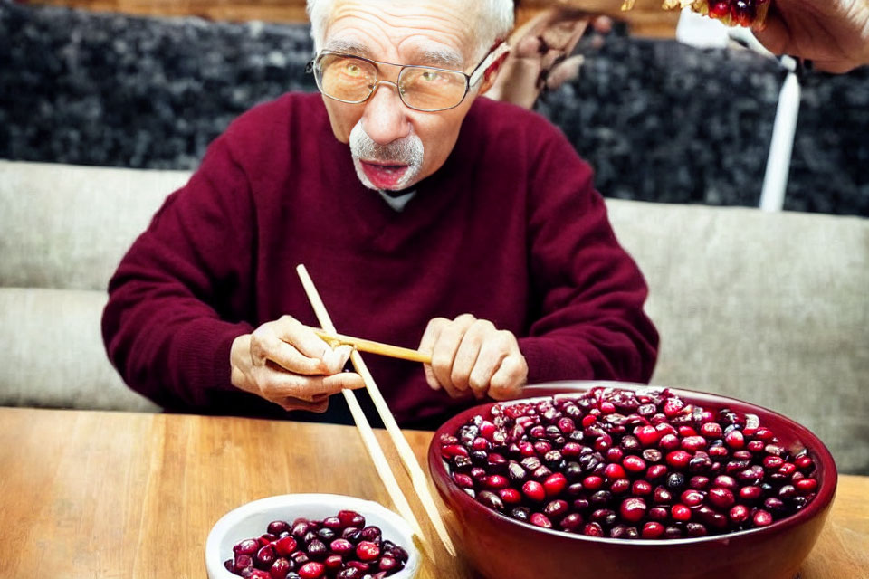 Elderly man eating cherries with chopsticks from large bowl