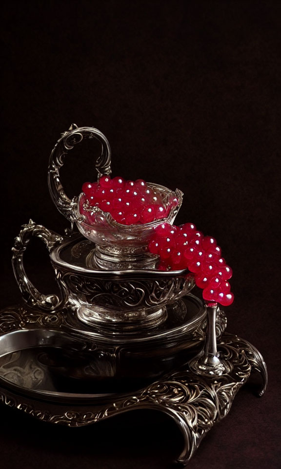 Silver tea set with intricate designs: saucer, teacup, and sugar bowl adorned with red