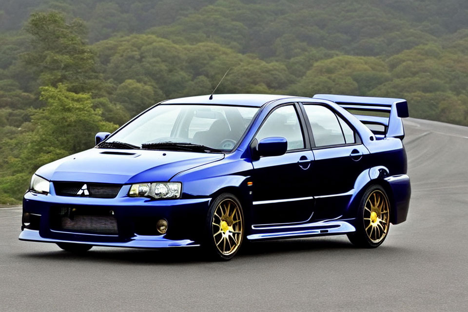 Blue sports sedan with large rear spoiler and yellow rims on road with greenery