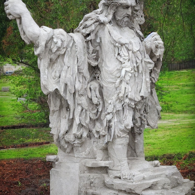 Stone statue of bearded figure in robes with outstretched arm in green background