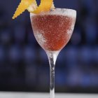 Red Cocktail with Sugar Rim, Lime Wedge, and Orange Peel on Blue Background