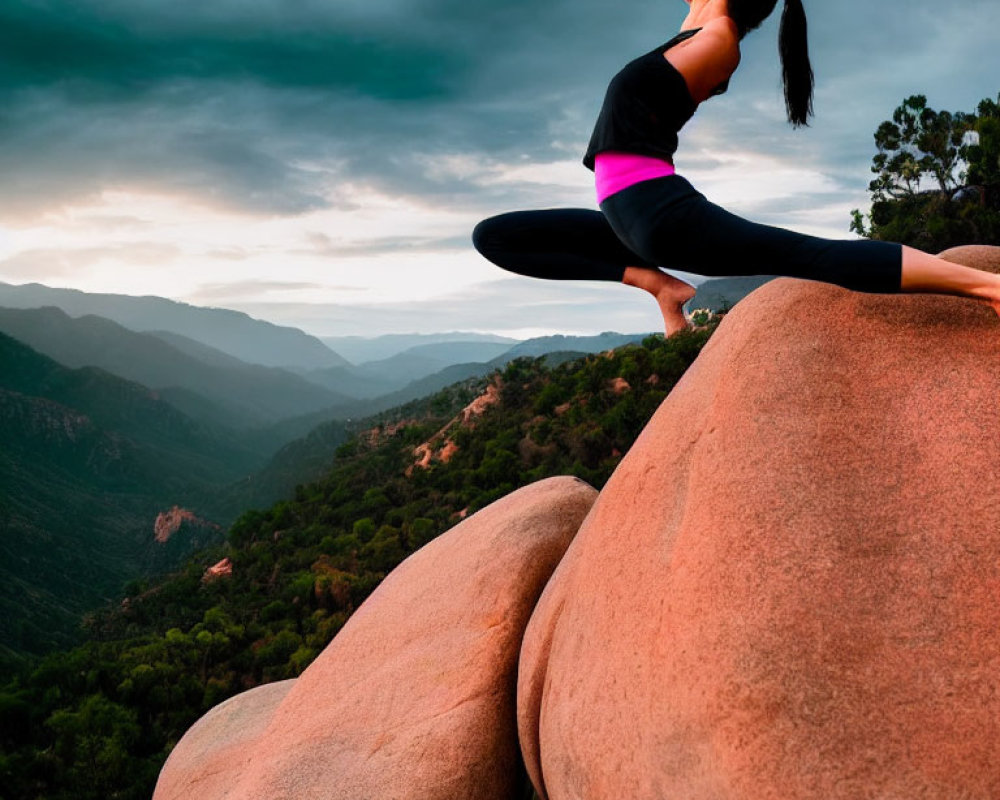 Woman practicing yoga on boulder with dramatic sky and mountains.