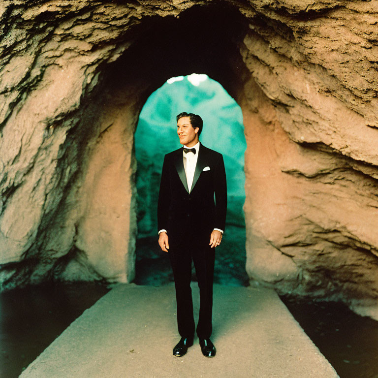 Man in formal black tuxedo posing in natural cave with arched entrance