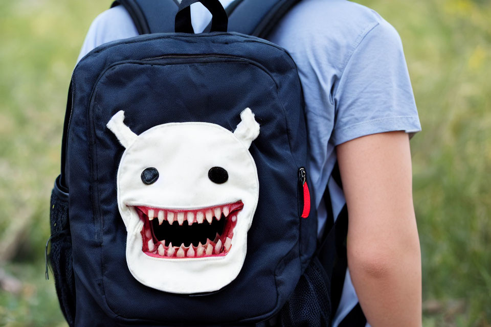 Blue Backpack with Cartoon Monster Face Design on Grass Background