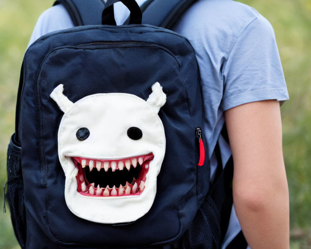 Blue Backpack with Cartoon Monster Face Design on Grass Background